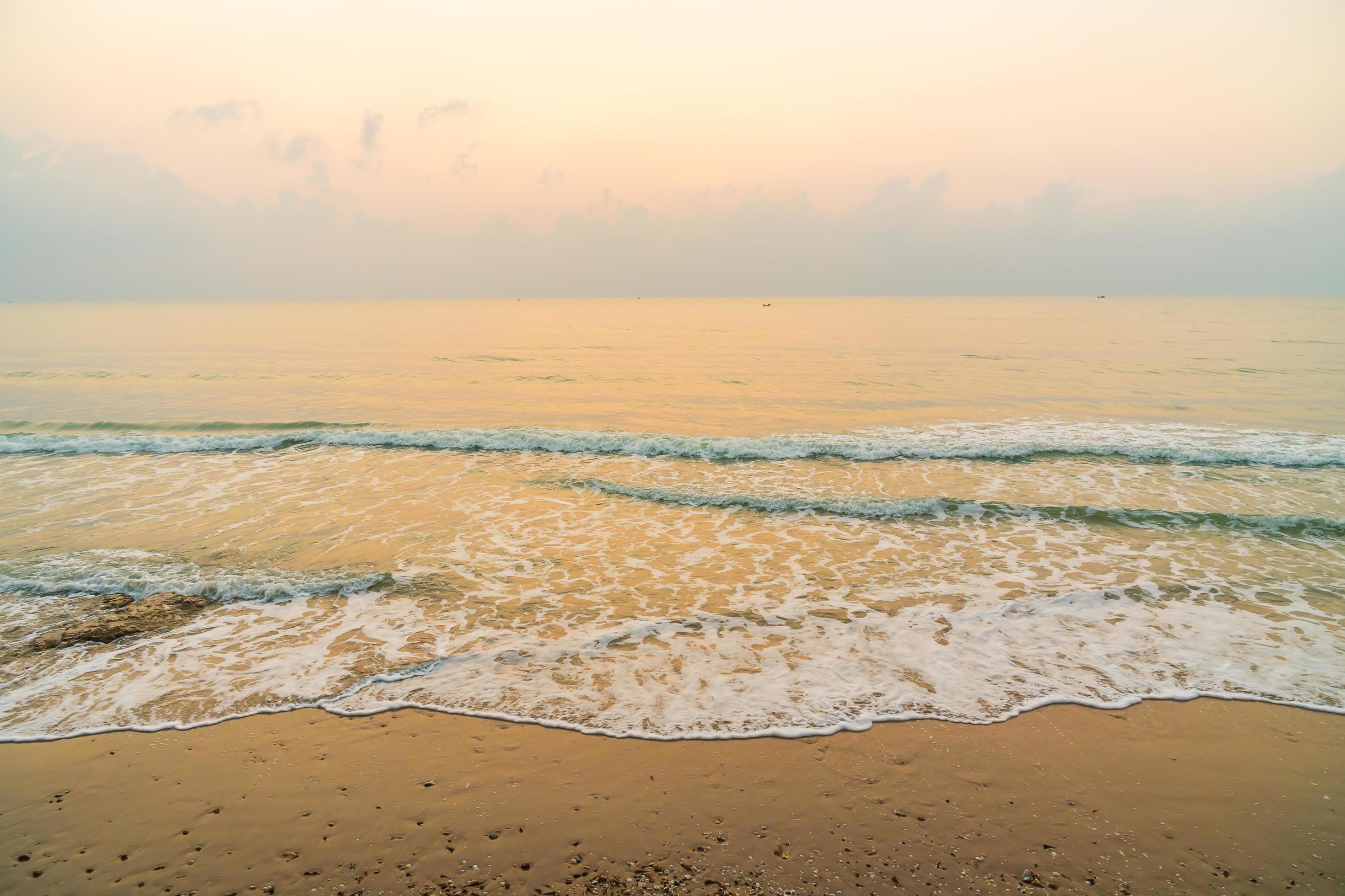 Wide view of a calm beach at sunrise with pale golden sky, gentle turquoise waves, and wet reflective sand